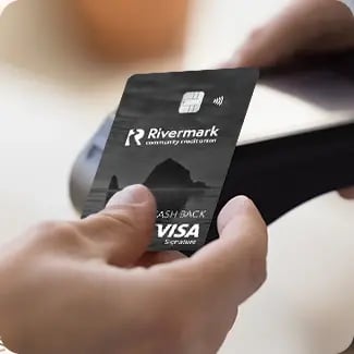 A close-up image of a person's hand using their credit card to make a tap payment on a card reader.