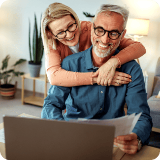 An older couple happily reviewing financial documents in front of a laptop computer.