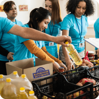 A group of volunteers at Sunshine Division helping pack groceries and items into a shopping cart for a customer.