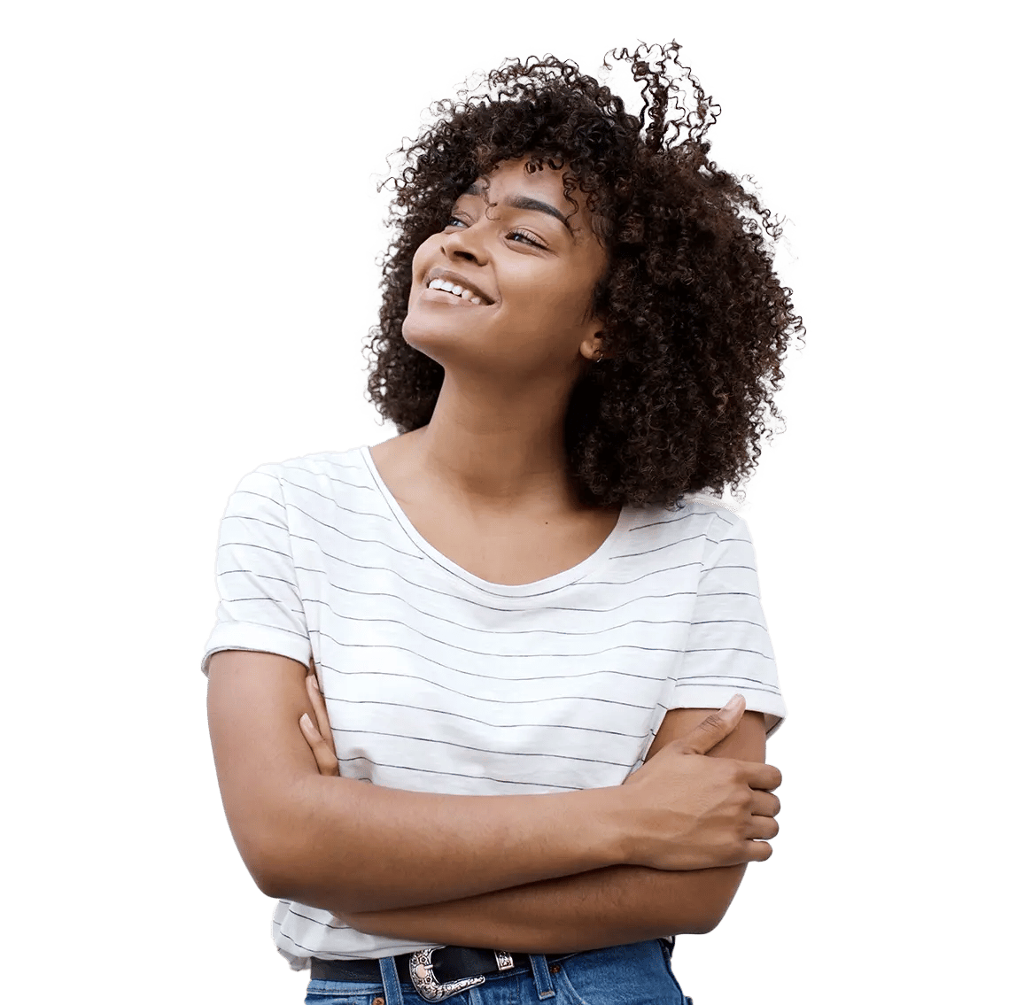 A person with curly hair smiles while standing with arms crossed, wearing a white striped T‑shirt and blue jeans, conveying quiet confidence.