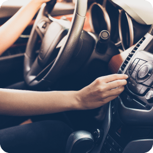 Hands holding a steering wheel in a car and turning up the volume.