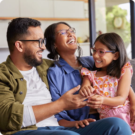 A happy family laughing with their daughter sitting on a couch together.