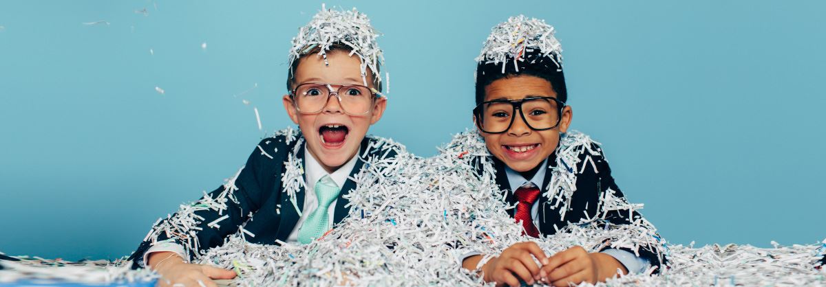 Two young boys sitting in a pile of shredded paper.