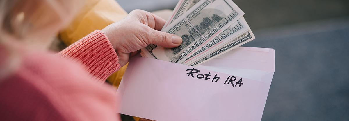 Money being pulled out of an envelope with Roth IRA written on it
