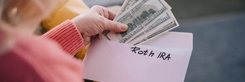 Money being pulled out of an envelope with Roth IRA written on it