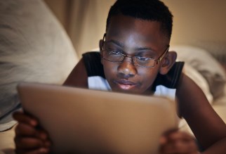 Young kid looking at a tablet on his bed.