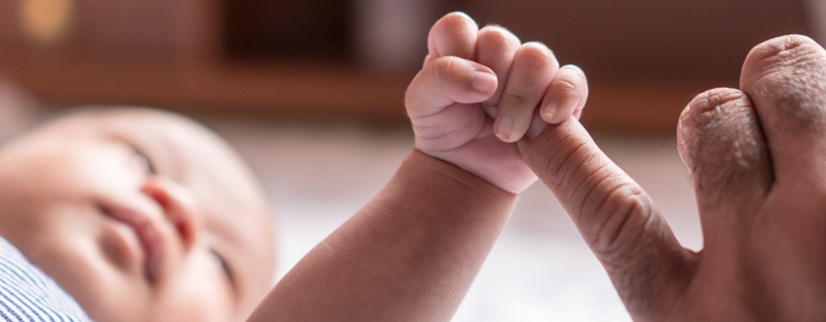 A tiny baby holding the finger of its parent.